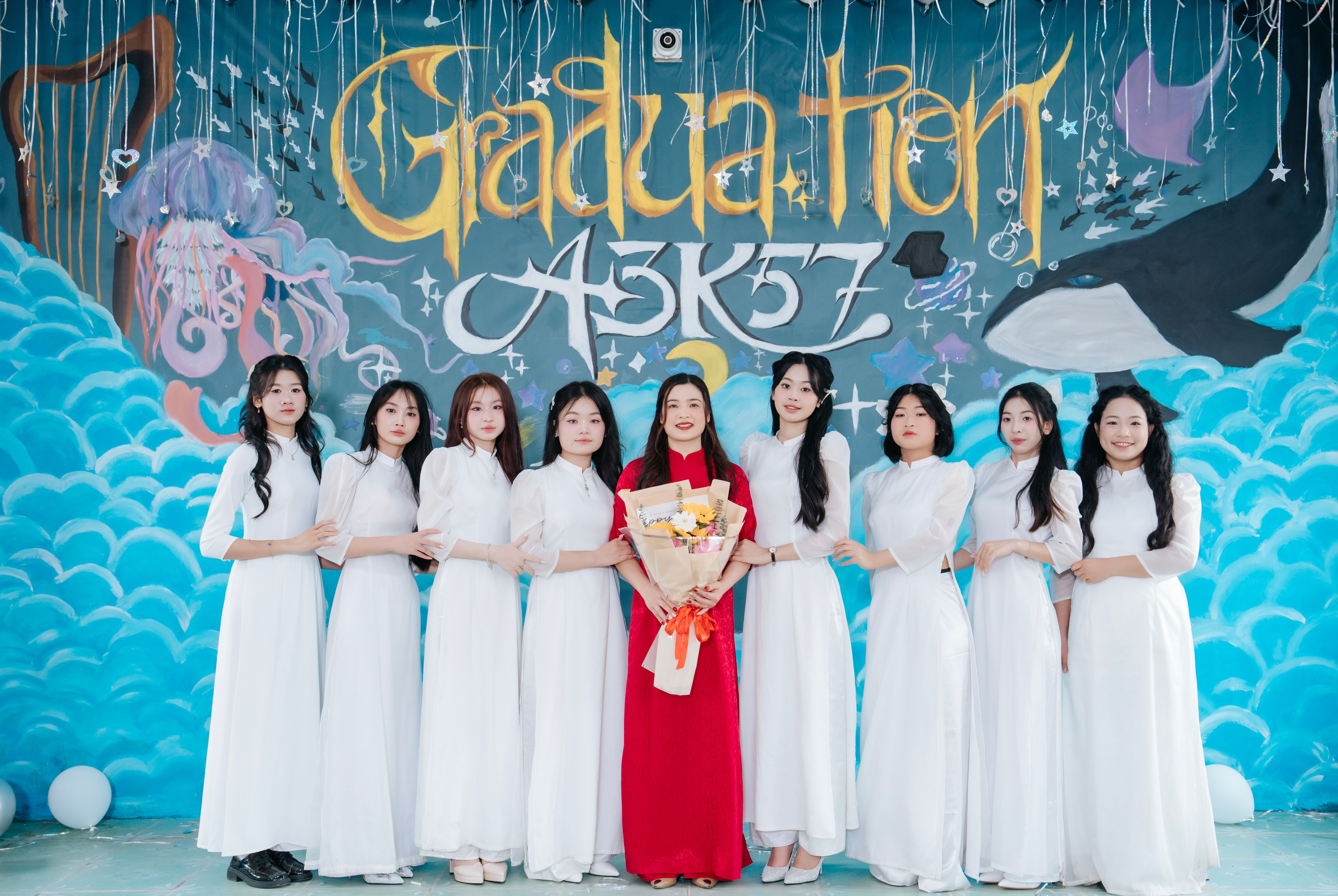 Group of women in traditional dresses celebrating graduation with a colorful backdrop.