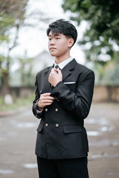 Youthful man in suit adjusting tie outdoors, exuding confidence