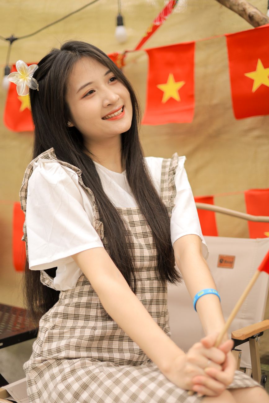 Young woman in checkered dress celebrates with Vietnamese flags indoors.