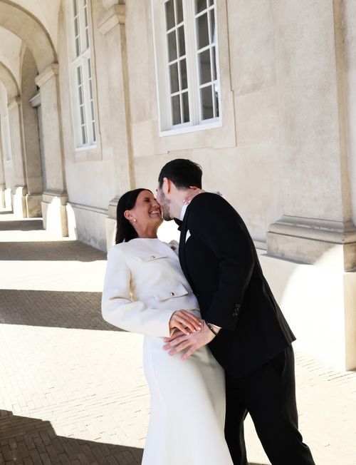 Free Romantic wedding couple sharing a joyful moment under historic arches in Copenhagen, Denmark. Stock Photo