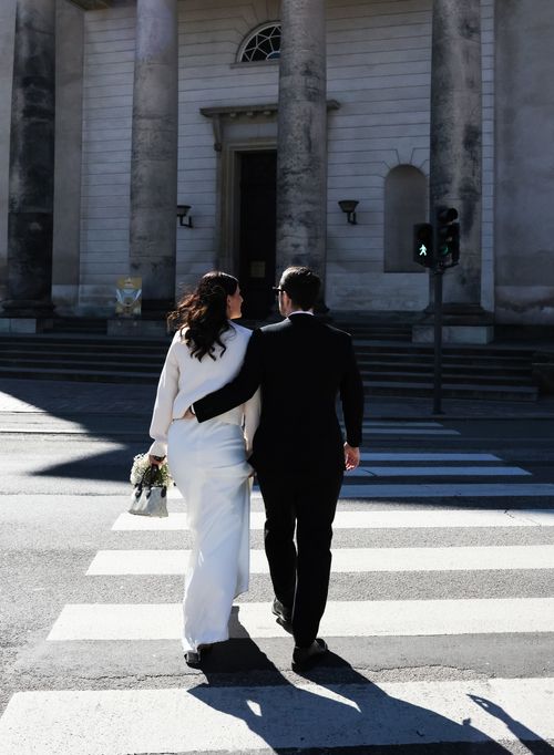 Free Bride and groom crossing a city street in Copenhagen, holding each other lovingly. Stock Photo