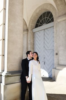 Bride and groom pose in elegant attire outside a classic archway in Copenhagen