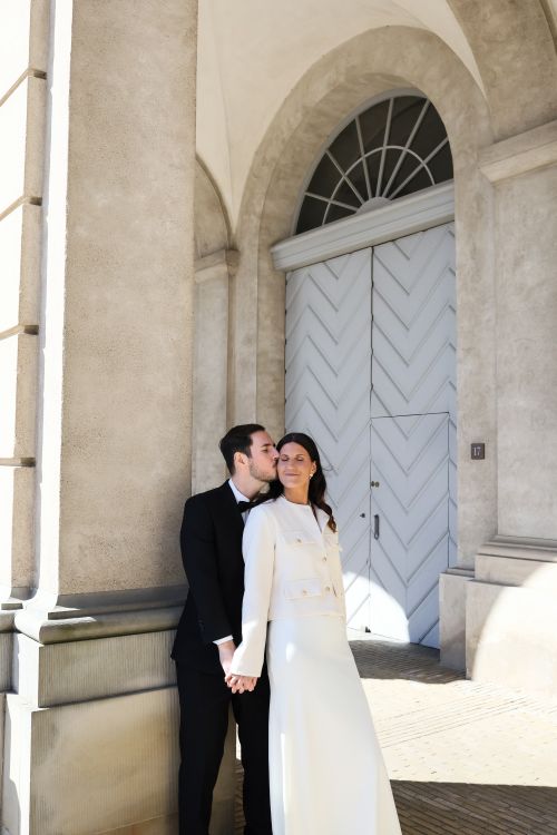 Free Bride and groom pose in elegant attire outside a classic archway in Copenhagen Stock Photo