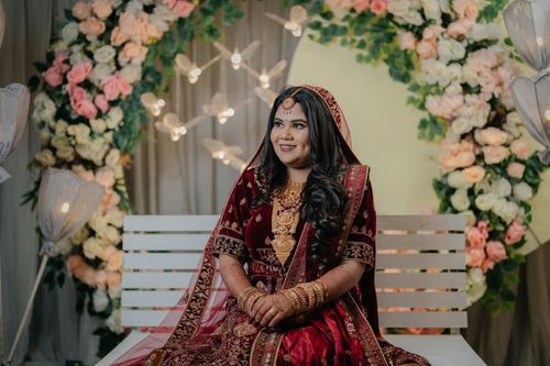 Free Indian bride in red traditional attire with floral backdrop, smiling elegantly. Stock Photo