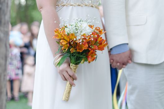 Bride holding vibrant flower bouquet during outdoor wedding ceremony, symbolizing love.