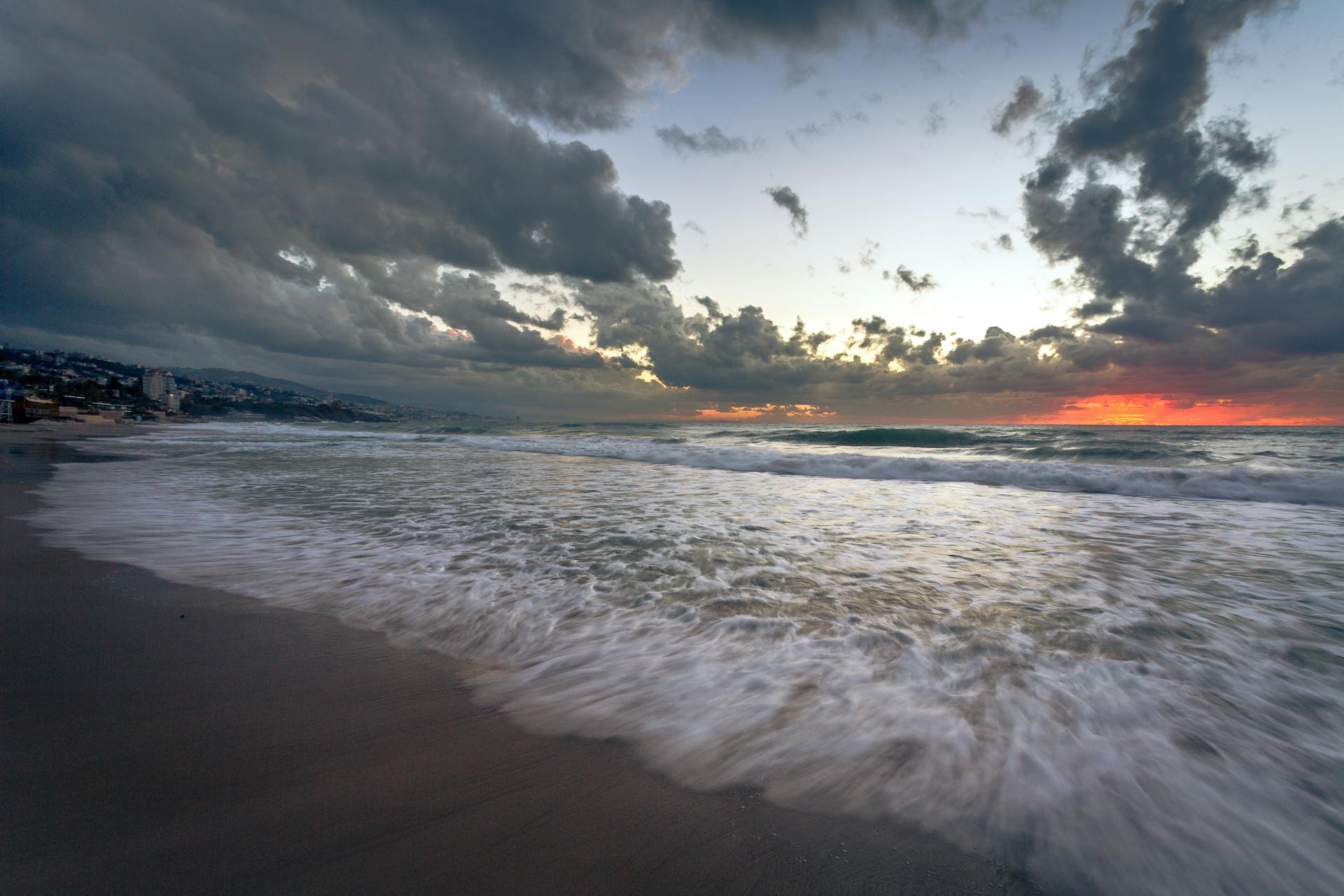 Stunning sunset view over the Byblos beach with dramatic clouds and ocean waves.