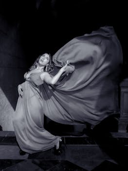Striking black and white portrait of a woman posing with a flowing gown, capturing elegance and movement.
