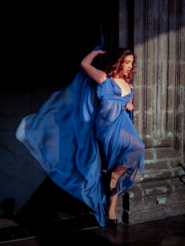 A woman in a flowing blue dress strikes a graceful pose against a stone wall in Ciudad de México.