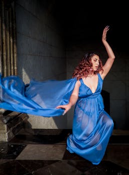 A woman in a flowing blue dress gracefully dances, capturing elegance and movement indoors.