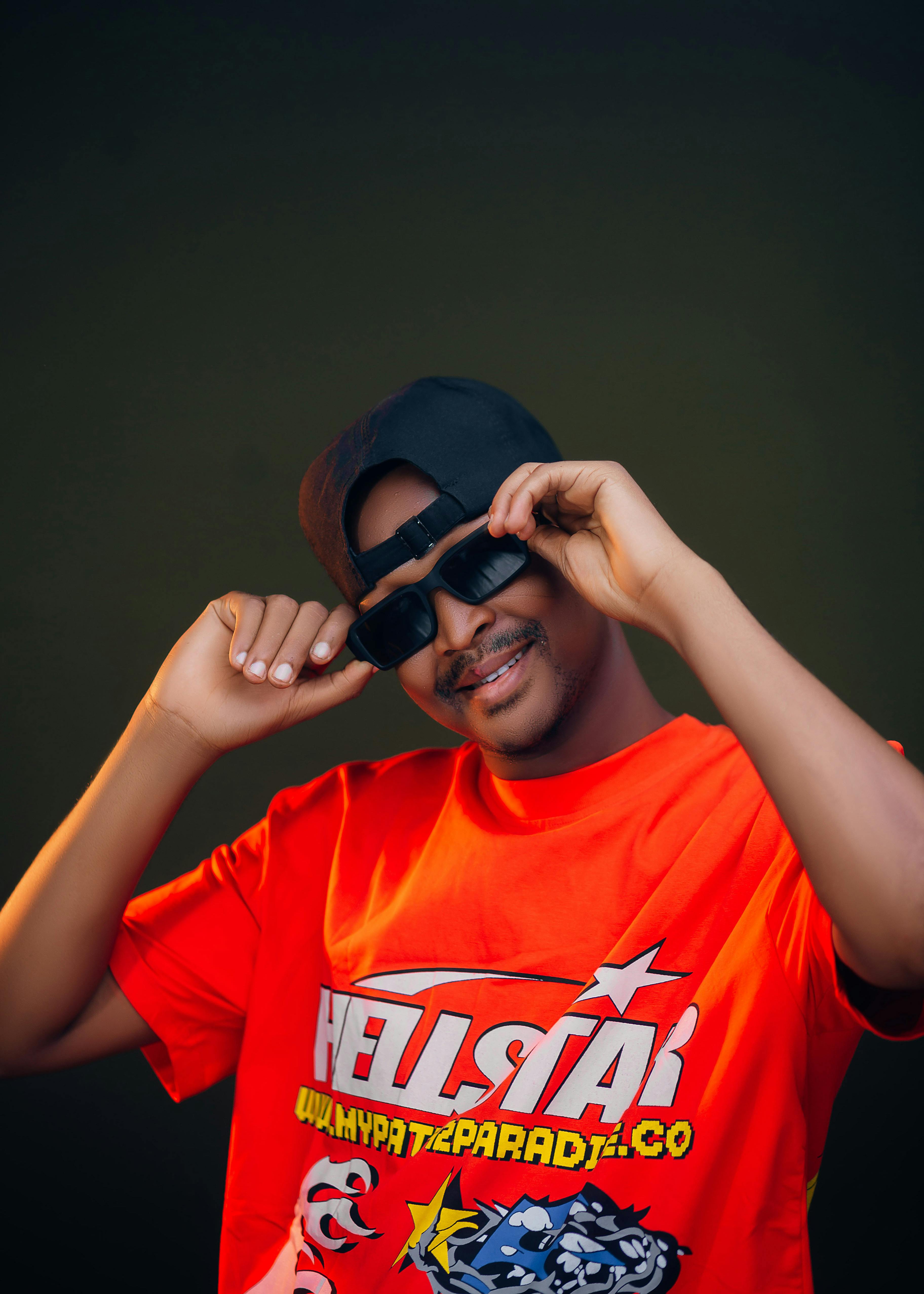 Young man wearing a red graphic T-shirt, cap, and sunglasses posing confidently indoors.