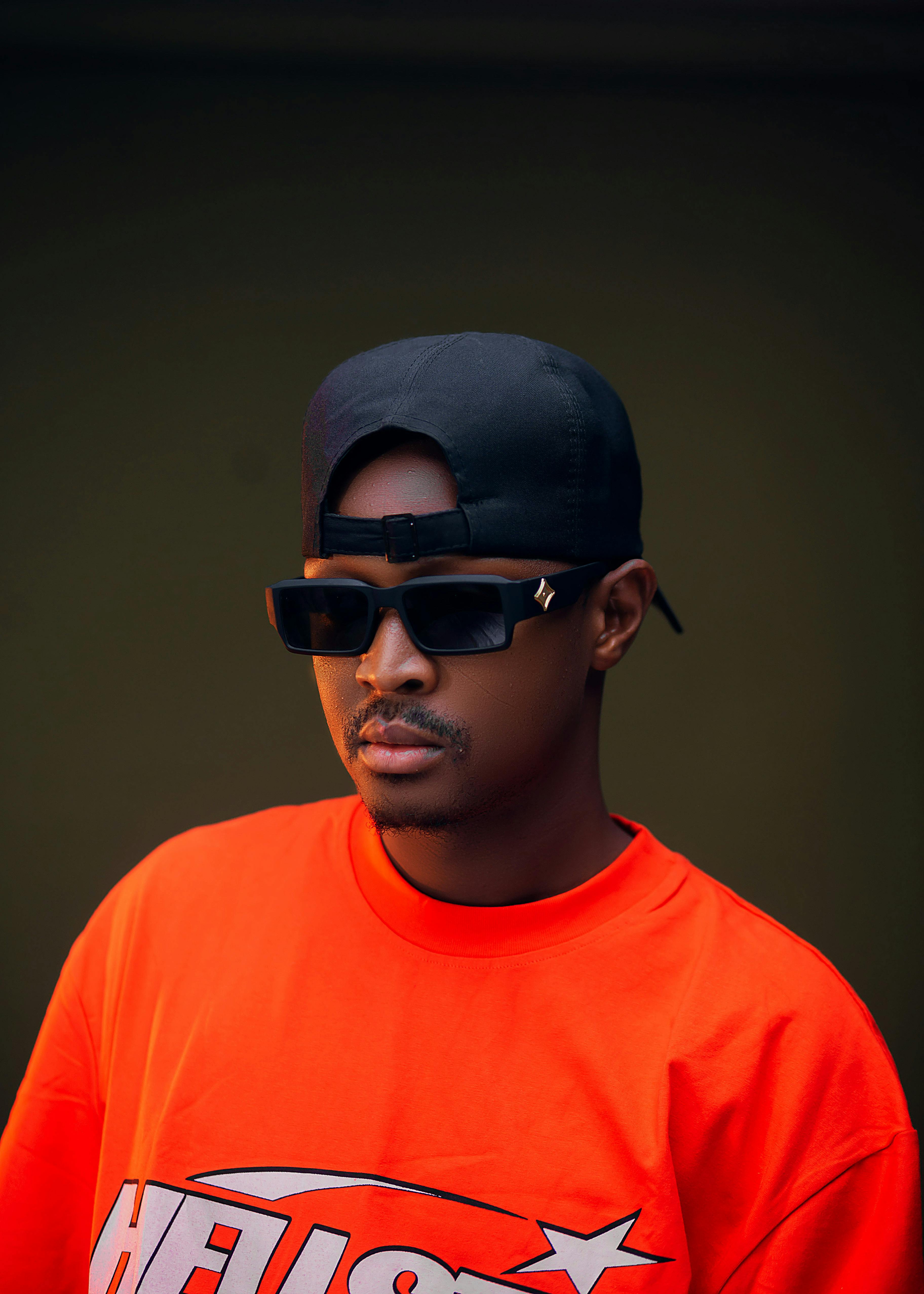 A fashionable young man wearing sunglasses and an orange t-shirt posing confidently indoors.