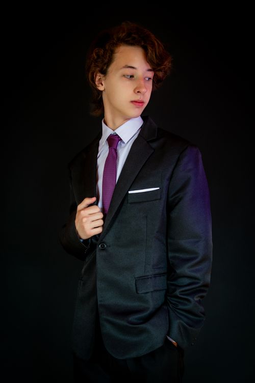 Free Elegant portrait of a young man in a dark suit and purple tie against a black background. Stock Photo