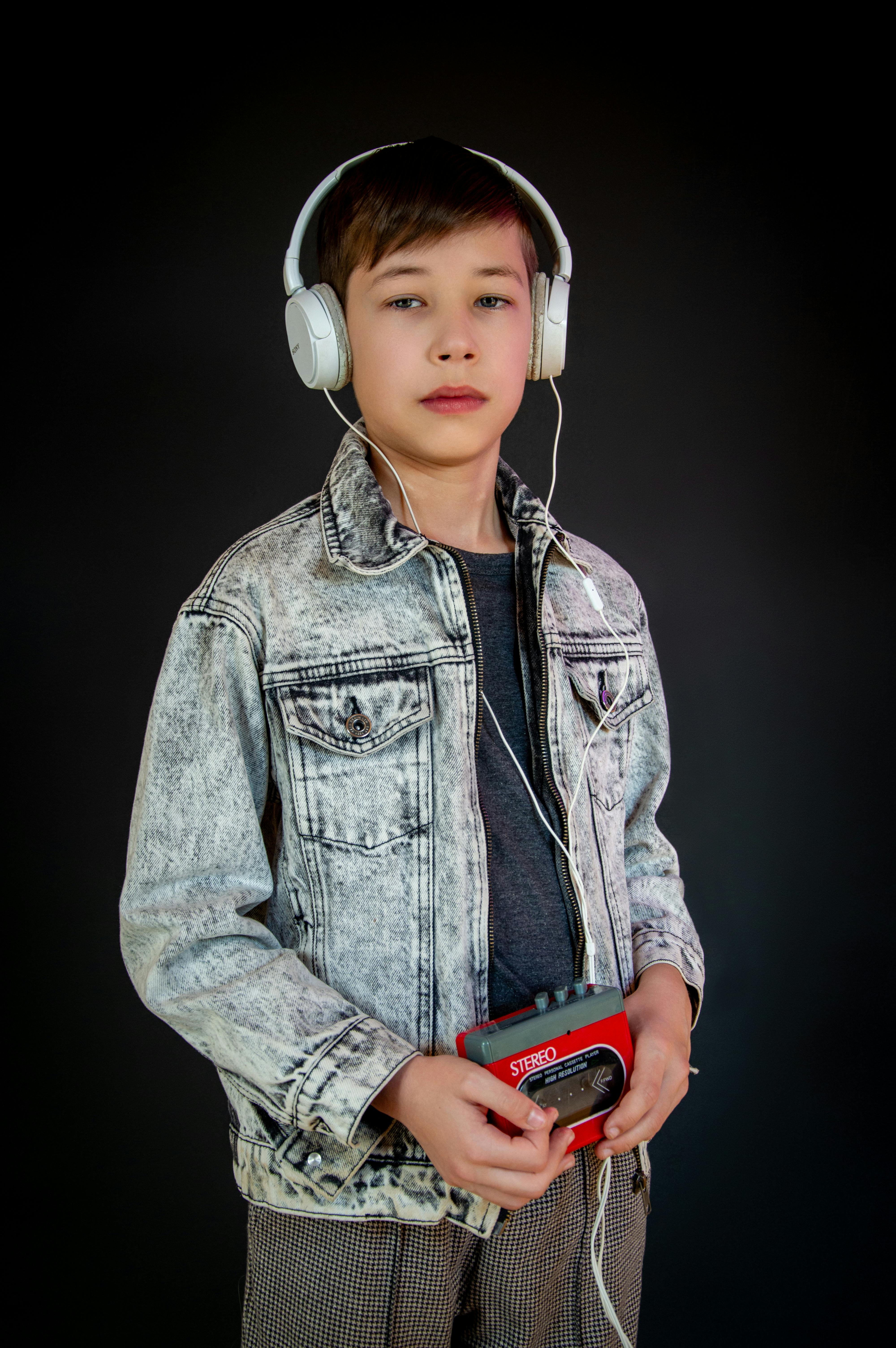 Gratis Un ragazzino che indossa le cuffie e tiene in mano un Walkman retrò su uno sfondo nero. Foto a disposizione