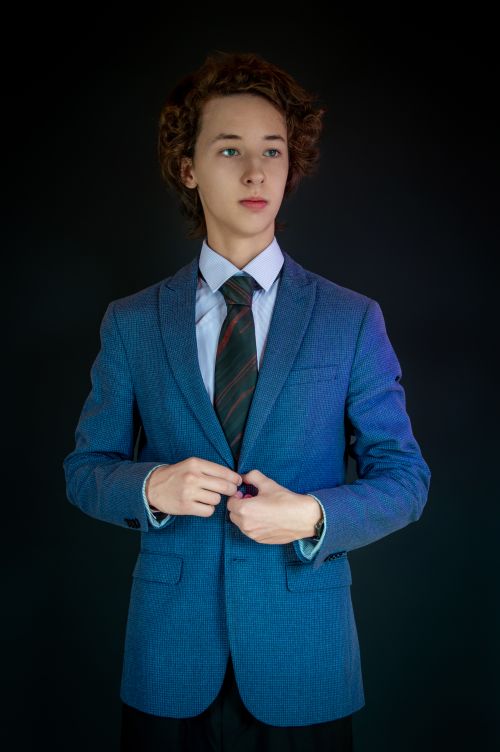 Free Portrait of a young man wearing a blue suit and tie, posing confidently against a black studio background. Stock Photo