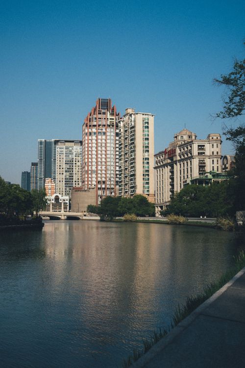 Free City skyline with diverse architecture reflecting on a tranquil river under clear blue skies. Stock Photo