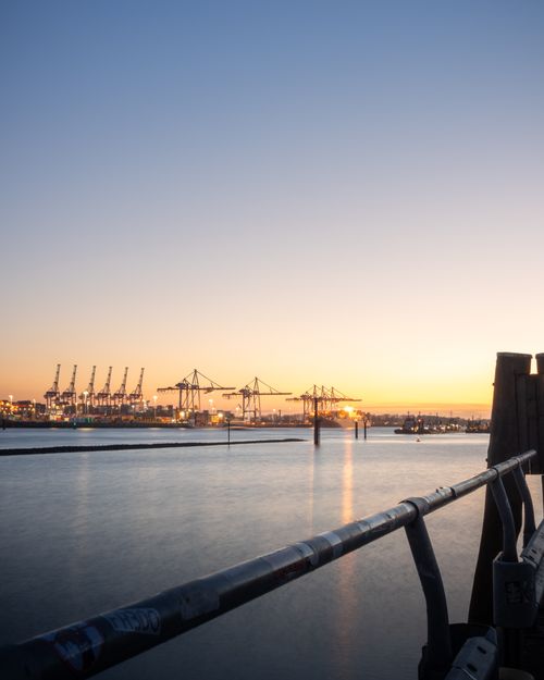 Free Scenic view of Hamburg port with cranes at sunset, tranquil waters reflecting the lights. Stock Photo