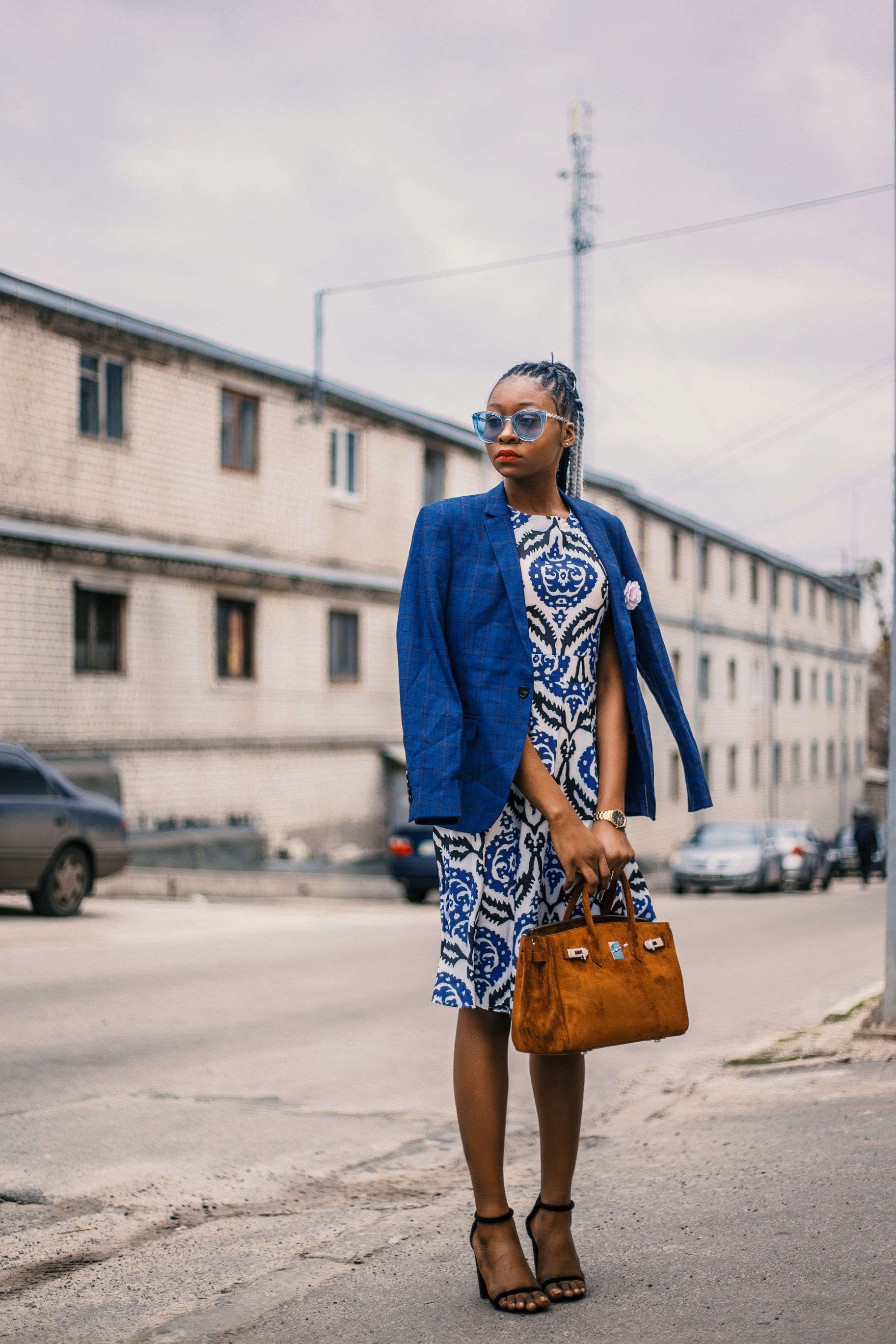 Mulher elegante em um vestido azul e blazer posando com confiança em uma rua da cidade.