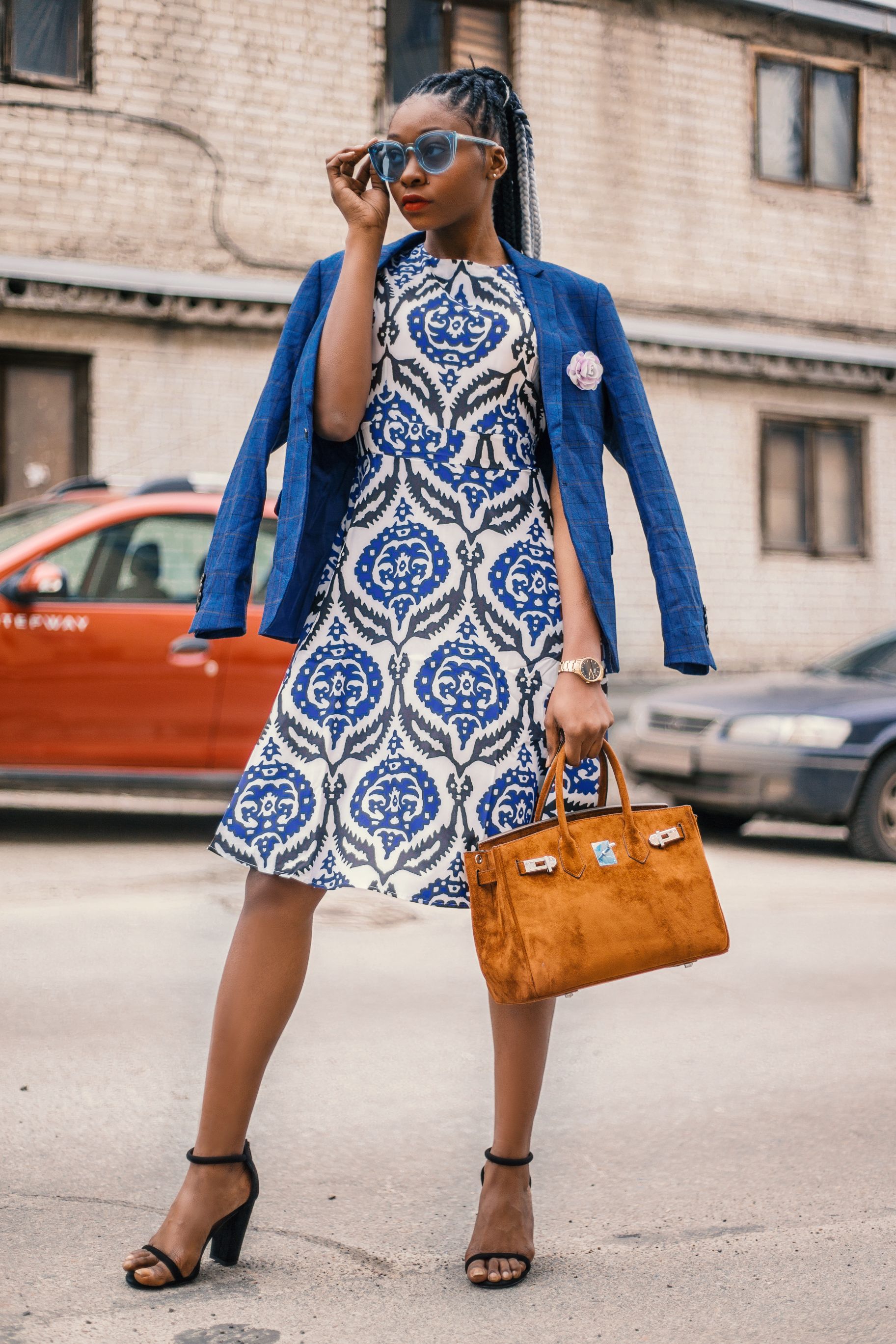 Mulher estilosa com blazer azul e vestido posando confiantemente ao ar livre.