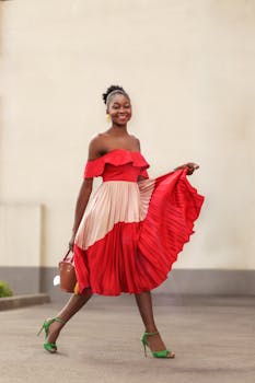 African woman in a vibrant red off-shoulder dress walks joyfully outdoors.