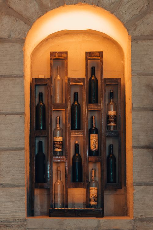 Free An elegant arrangement of wine bottles displayed in a rustic brick alcove with warm lighting. Stock Photo