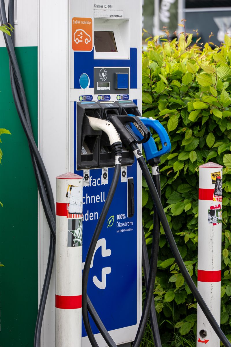 Close-up of an electric vehicle charging station outdoors surrounded by greenery, showcasing clean energy technology.