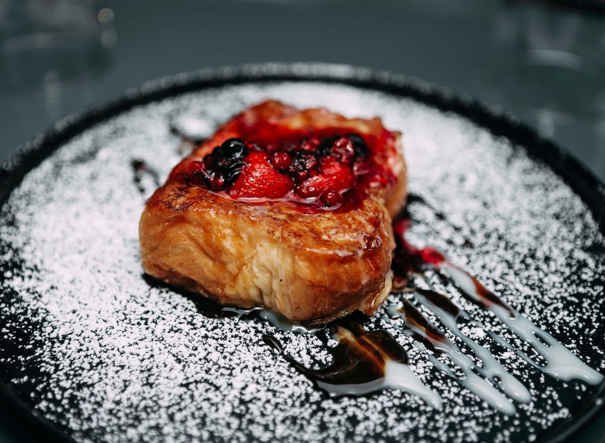 French toast topped with fresh berries and powdered sugar on a dark plate
