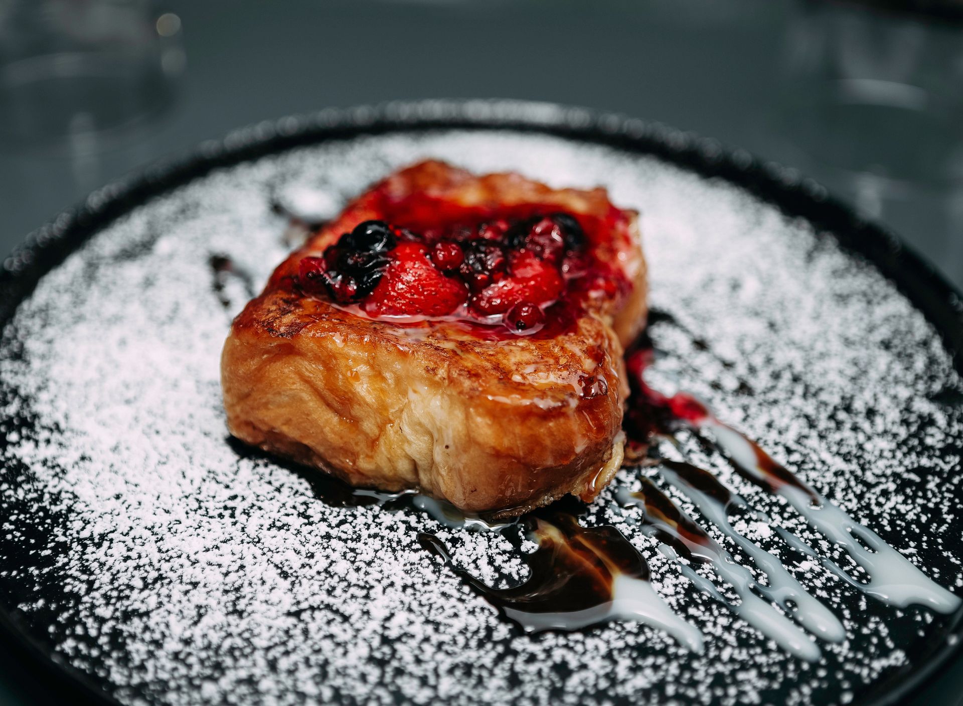 Close-up of french toast topped with fresh berries, powdered sugar, and syrup on a plate.