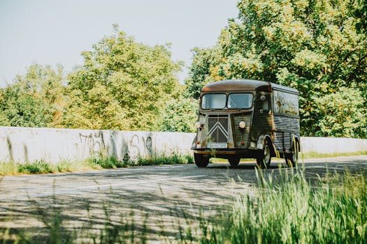 Classic Citroën HY van driving on a scenic road surrounded by lush greenery on a sunny day.