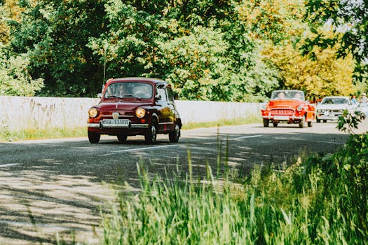 Classic cars driving on a picturesque country road surrounded by lush greenery.