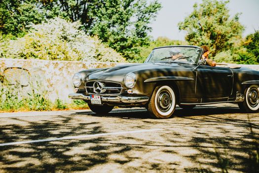Classic convertible car cruising through a vibrant, sunny landscape.