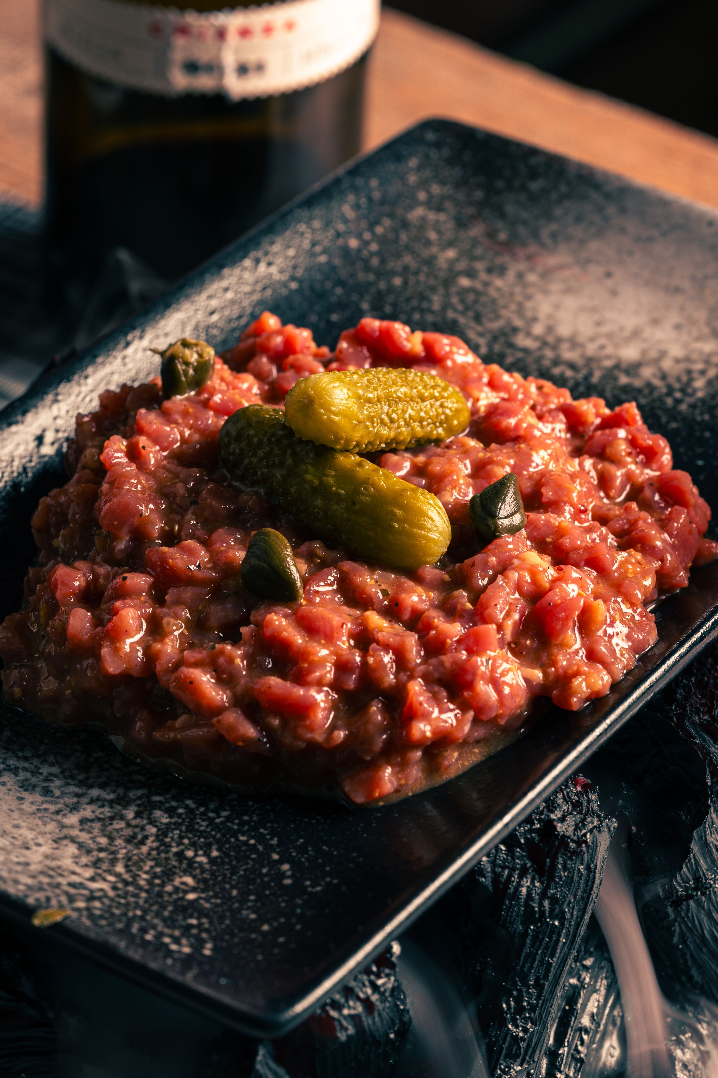 Close-up of a savory beef tartare with pickles on a modern plate.