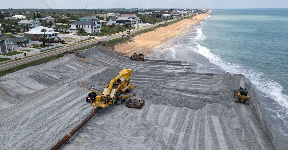 Aerial view of beach restoration with heavy machinery and coastal homes.