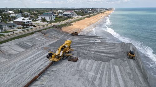 Free Aerial view of beach restoration with heavy machinery and coastal homes. Stock Photo