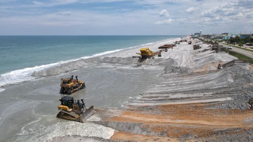 Free Aerial view of beach restoration work with bulldozers reshaping the coastline. Stock Photo