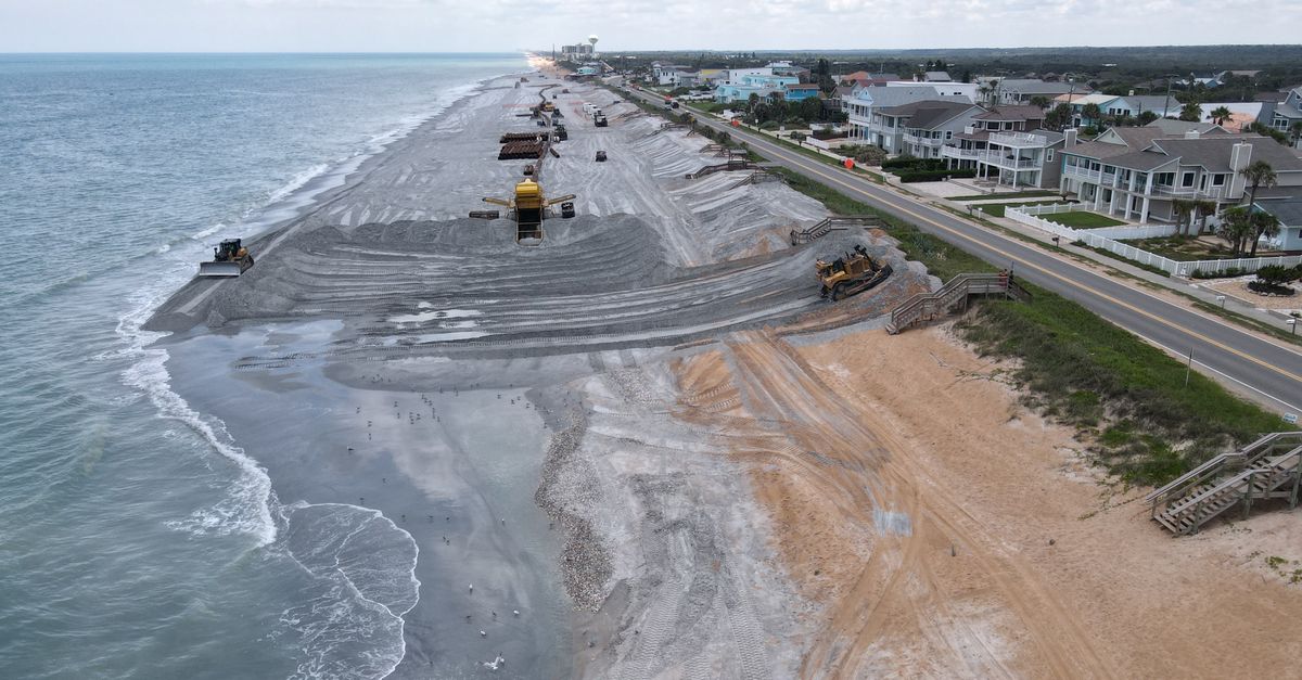 Aerial view of a beach restoration project with construction vehicles on the coastline.