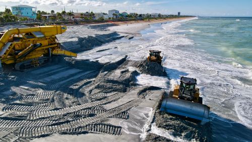 Free Heavy machinery working on beach coastline to manage erosion and restore sand. Stock Photo