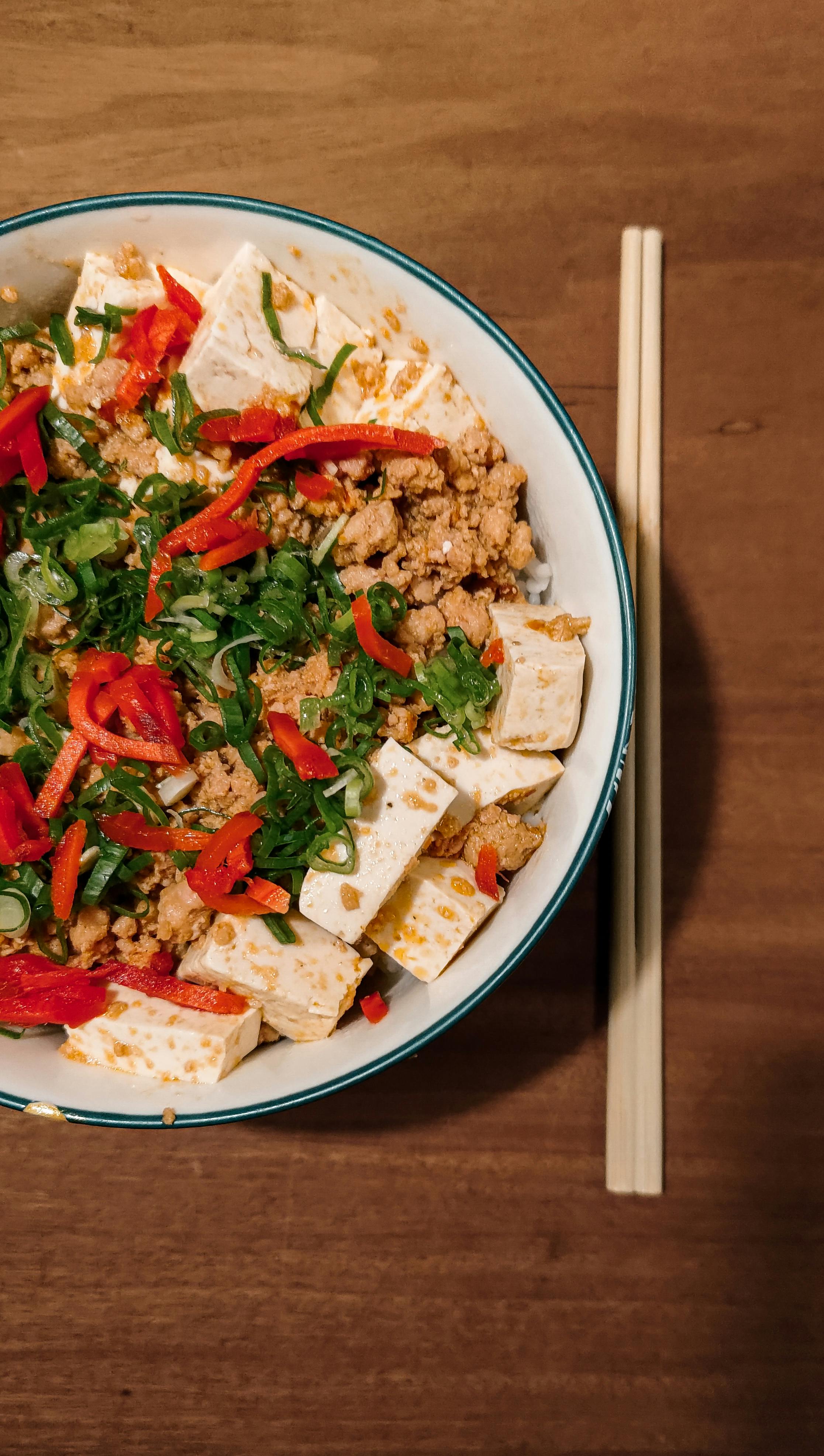 Bowl of mapo tofu with silky white tofu cubes in bright red mala sauce garnished with green scallions