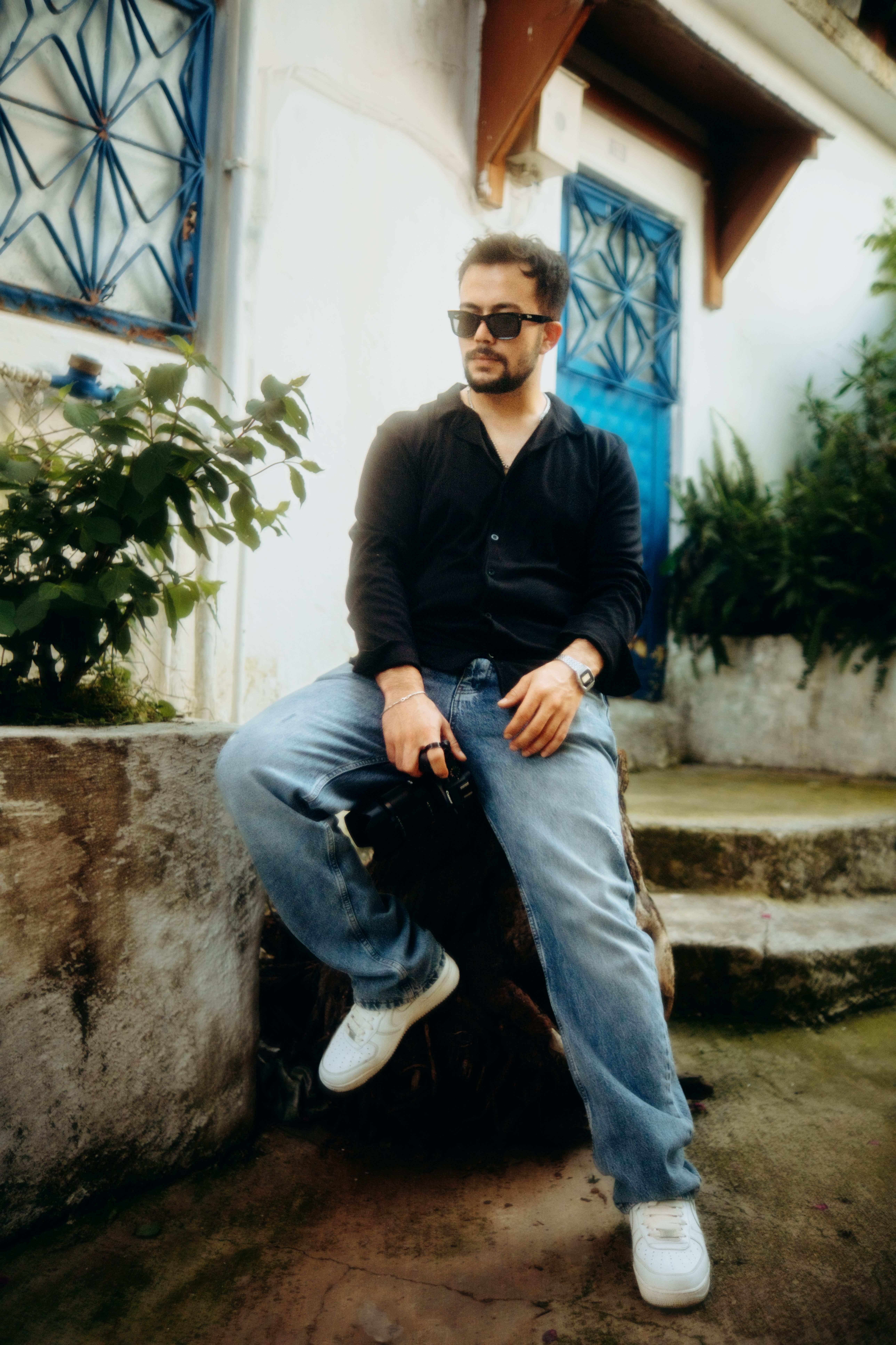Stylish man in sunglasses sitting outdoors, exuding confidence and urban vibe.