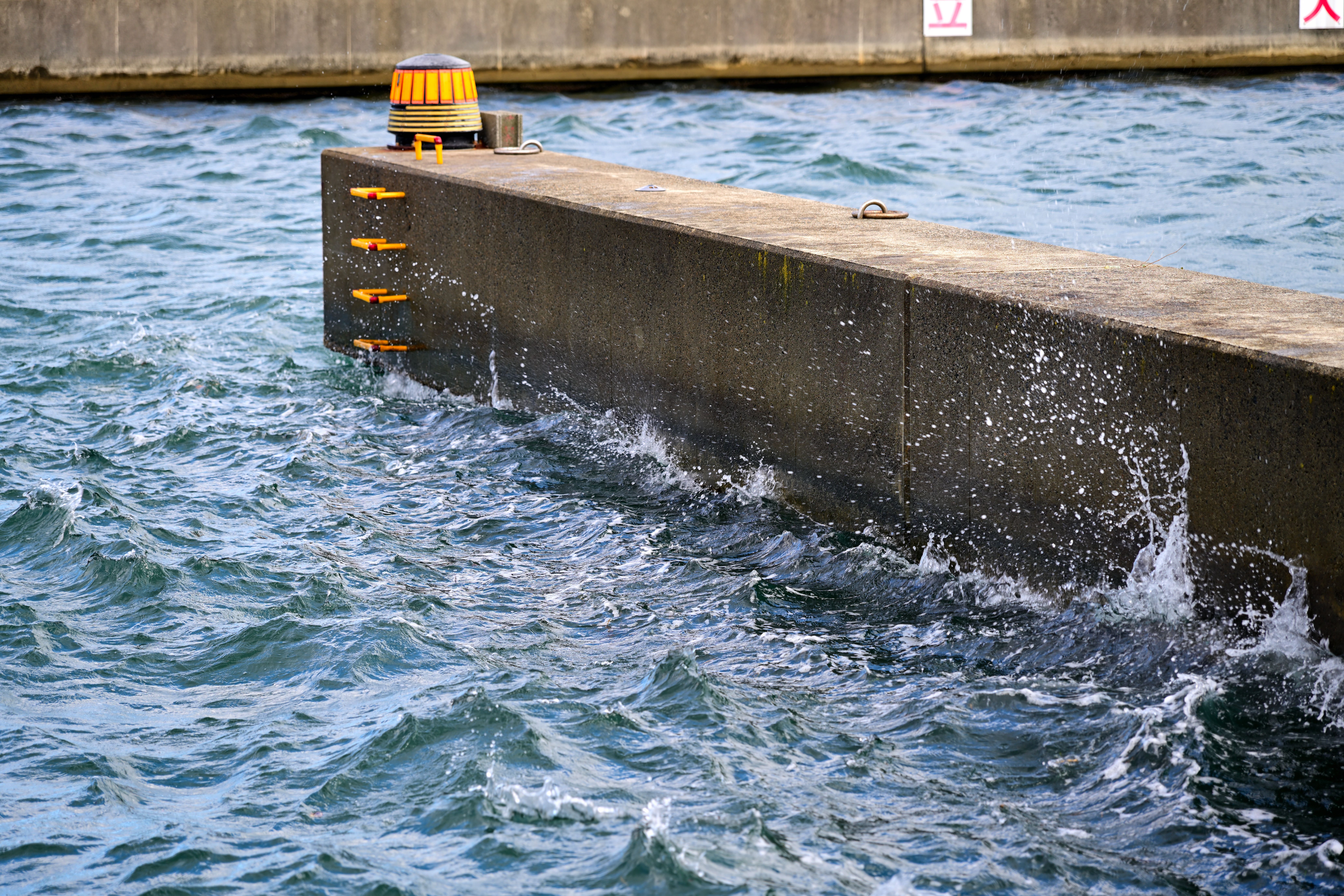 Dynamic waves crash against a pier wall, creating a dramatic water splash.