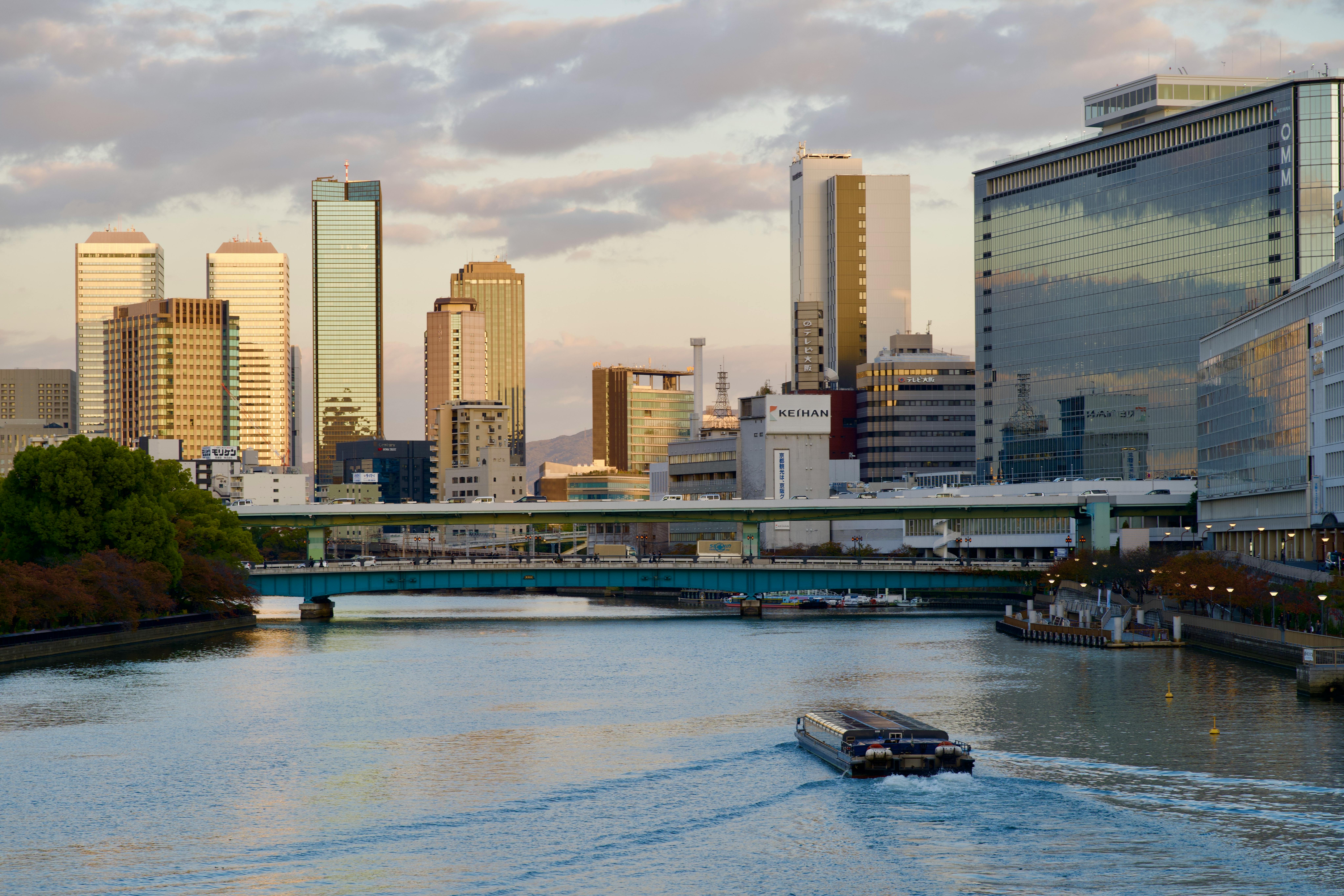 Scenic view of Osaka skyline and river during a calm day. Reflective high-rises and tranquil water create a serene atmos