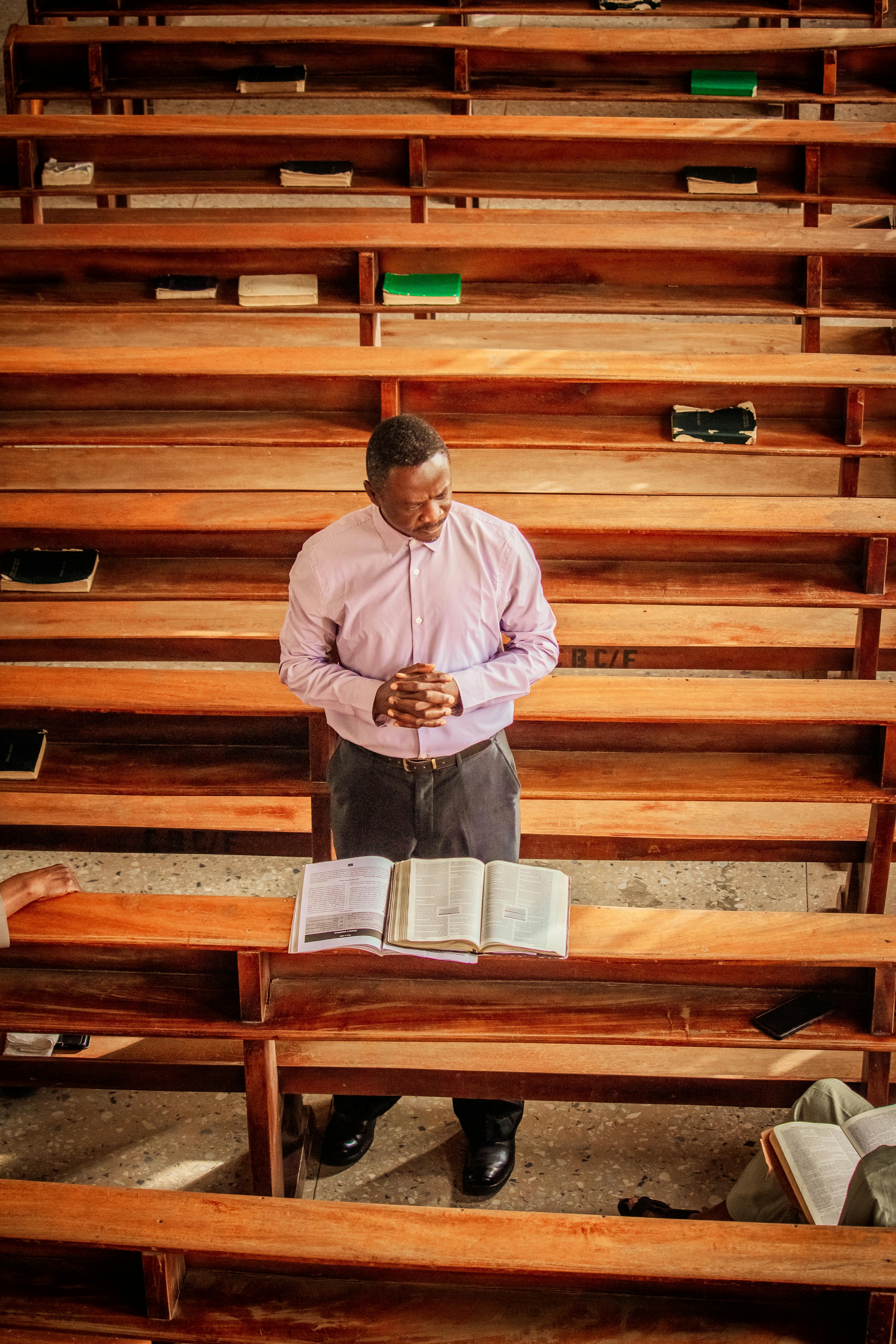 A solitary man prays with a Bible open in wooden church pews, creating a serene and spiritual atmosphere.