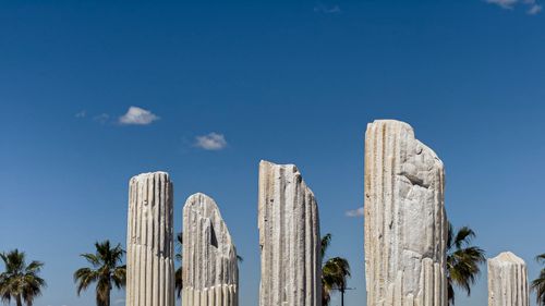 Free Scenic view of ancient stone columns with palm trees and a clear blue sky. Stock Photo