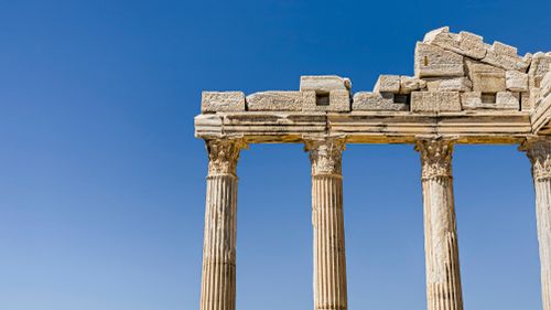 Free Columns of an ancient Greek temple stand tall against a bright blue sky. Stock Photo