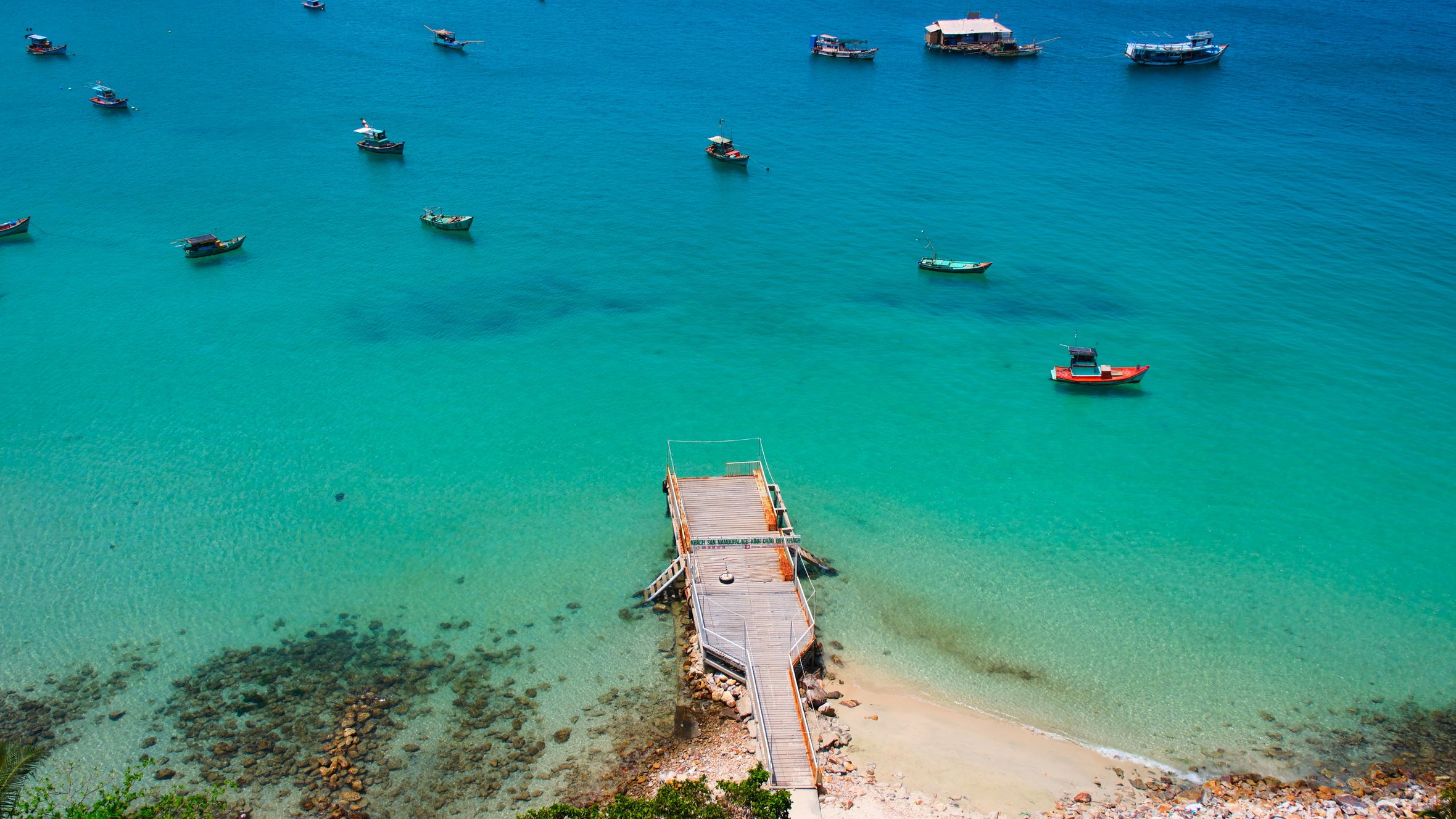 Stunning aerial view of a dock surrounded by boats and crystal-clear blue ocean water.