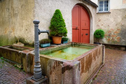 Free Rustic fountain in a courtyard with stone walls and red door in Sankt Pauls, Italy. Stock Photo