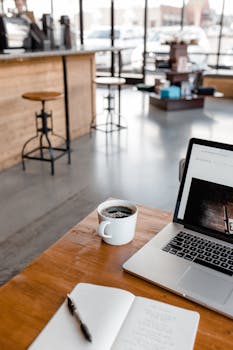A peaceful workspace in a coffee shop with a laptop, journal, and coffee cup.
