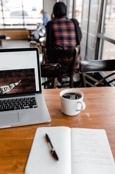 Laptop, coffee, and notebook setup for remote work in a cozy coffee shop.