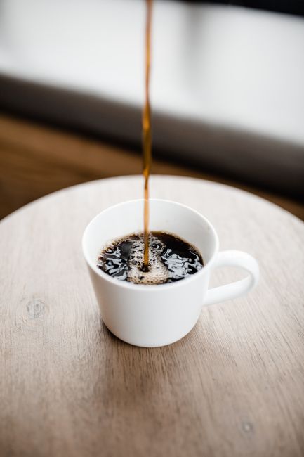 A small glass pitcher of homemade half and half being poured into a cup of coffee, with a measuring cup of whole milk and heavy cream in the background.