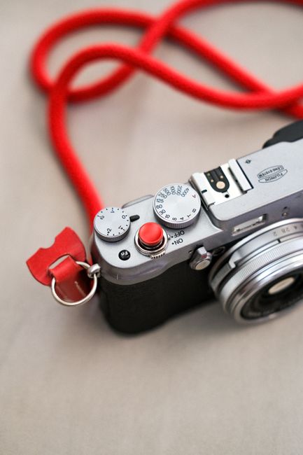 Close-up image showcasing a vintage-style camera with a striking red strap on a neutral surface.