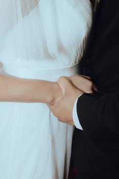 Close-up of a bride and groom holding hands, highlighting intimacy and elegance on their wedding day.